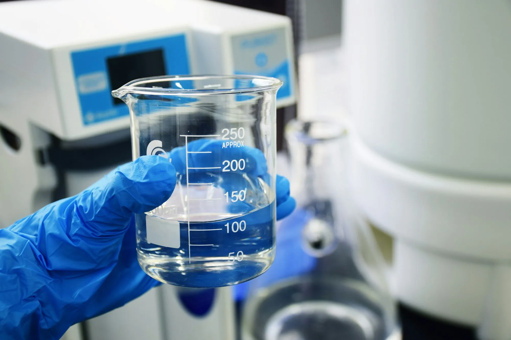 A gloved hand holding a beaker of water for testing